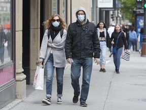 People with face masks and without face masks walk along Sainte-Catherine street in Montreal, Sunday, May 31, 2020, as the COVID-19 pandemic continues in Canada and around the world. new poll suggests Americans are more convinced than their Canadian counterparts that a second, more powerful wave of COVID-19 is on its way.