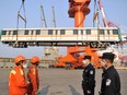 Police officers and dock workers wear face masks to prevent the spread of COVID-19, as they stand near a railway carriage being shipped to Singapore, at a port in Qingdao, China, on March 18.