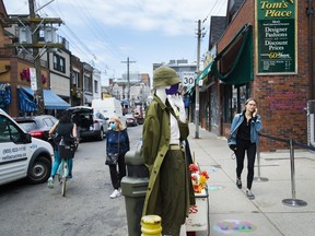People walk by a mannequin wearing a mask as store fronts open up for business in Kensington Market during the COVID-19 pandemic in Toronto on Tuesday, June 2, 2020.