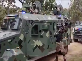 Members of the CJNG pose in front of armoured vehicles.