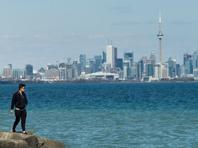 A man walks on rocks by Lake Ontario with the downtown core in the backdrop in Toronto on Monday, April 27, 2020.