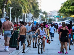 A man rides a bicycle as people walk on Ocean Drive in Miami Beach, Florida on June 26, 2020.