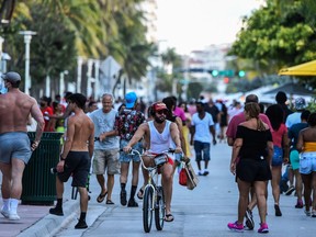 A man rides a bicycle as people walk on Ocean Drive in Miami Beach, Florida on June 26, 2020.