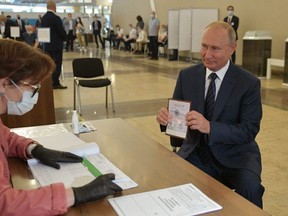 Russian President Vladimir Putin shows his passport to a member of a local electoral commission as he arrives to cast his ballot in a nationwide vote on constitutional reforms at a polling station in Moscow on July 1, 2020.