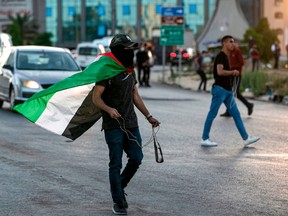 A masked Palestinian protester draped in a Palestinian flag walks with a slingshot during clashes with Israeli security forces, following a demonstration against Israel's potential plan to annex parts of the West Bank, in Ramallah on July 1.