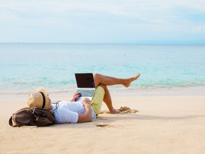 A man works on the beach, while lying on his bag.