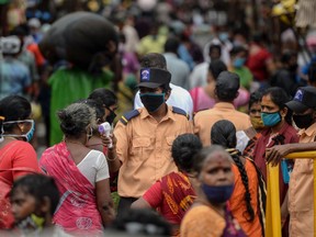 A security personnel (C) checks the body temperature of a woman (C-L) as she enters a market among a crowd of people as a preventive measure against the spread of the COVID-19 coronavirus in Chennai on July 29, 2020.