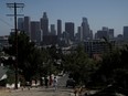 Pedestrians walk in front of the Los Angeles skyline in Los Angeles, on July 7.