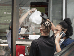 A Jerk King restaurant employee wearing a mask serves a customer through a takeout window on Toronto.