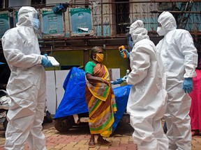 Medical volunteers wearing Personal Protective Equipment (PPE) gear take temperature reading of a woman as they conduct a door-to-door medical screening inside Dharavi slums to fight against the spread of the COVID-19 coronavirus, in Mumbai on July 9, 2020.