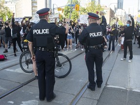 Police officers look on as protesters march in an anti-racism rally in Toronto on Saturday, June 6, 2020.