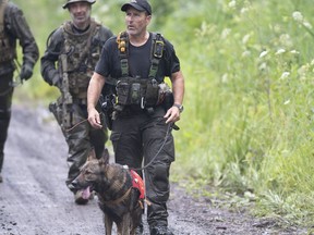 A K9 unit and other police officers search a back road on Saturday, July 11, 2020 in St-Apollinaire, Que. Quebec provincial police continued to search through the night for the father of two girls whose bodies were found Saturday in a small town southwest of Quebec City.THE CANADIAN PRESS/Jacques Boissinot