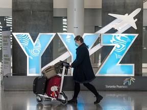 A woman wears a mask as she wheels luggage through Pearson International Airport's Terminal 1 in Toronto during the COVID-19 pandemic, on May 20, 2020.