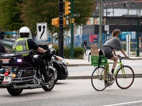 A member of the Vancouver Police traffic section that was providing an escort with other officers, rides behind a person on a bike participating in a roving protest against racism, in Vancouver, on Sunday, June 21, 2020. Vancouver council has voted unanimously to ban street checks because of overwhelming racial profiling, but the Vancouver Police Board, not council, has the final say on any decision about the checks.