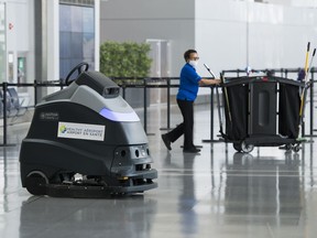 A automated floor cleaner that sanitizes the floor is shown as a worker walks by at Pearson International Airport during the COVID-19 pandemic in Toronto on Tuesday, June 23, 2020. Hospitality workers are calling on various levels of the government to work creatively and avoid long-term unemployment in the sector.
