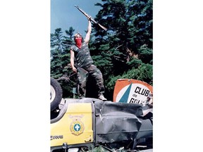 A warrior raises his weapon as he stands on an overturned police vehicle blocking a highway at the Kahnesetake reserve near Oka, Que., July 11, 1990 after a police assault to remove Mohawk barriers failed.