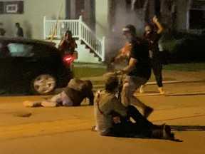 A man is shot at by a person sitting on the street during a protest following the police shooting of Jacob Blake, a Black man, in Kenosha.