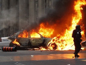 Riot police pass a Toronto Police cruiser set ablaze by anti-G20 protesters at King and Bay Streets, Toronto, in June 26, 2010.