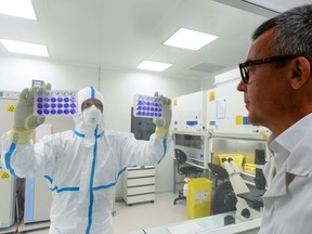 Valneva SE biotech company President and Chief Business Officer Franck Grimaud (R) looks at engineer-virologist Thomas Mollet, presenting two 24 well plates adherent cells monolayer infected with a Sars-CoV-2 virus in the Biosafety level 3 laboratory (BSL3) at the Valneva Group headquarters in Saint-Herblain, near Nantes, western France on July 30, 2020.