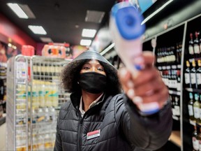 A liquor store worker measures temperatures of customers at the entrance of a shop in Melville, Johannesburg, on August 18, 2020. South Africa moved into level two of a five-tier lockdown on August 18, 2020, to continue efforts to curb the spread of the COVID-19 coronavirus. Under level two liquor and tobacco sales will resume.