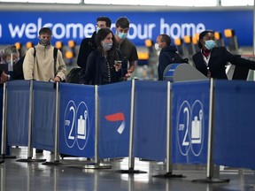 Passengers wearing face masks or covering due to the COVID-19 pandemic, queue at a British Airways check-in desk at Heathrow airport, west London, on July 10, 2020.