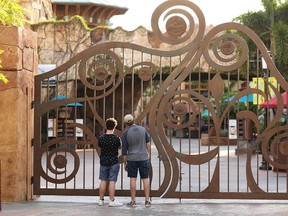 In this Thursday, May 14, 2020, file photo, guests peer through the closed gate to Universal's Islands of Adventure beside Universal CityWalk, in Orlando, Fla.
