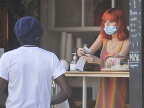 A woman wears a face mask as she gives a customer change at a cafe in Montreal, Sunday, August 16, 2020, as the COVID-19 pandemic continues in Canada and around the world.