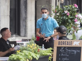 A server wears a face mask as he talks to customers at a restaurant in Montreal, Saturday, Aug. 22, 2020.