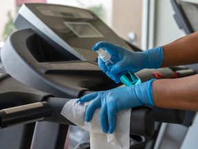 Staff using wet wipe and a blue sanitizer from the bottle to clean treadmill in gym. Antiseptic,disinfection ,cleanliness and healthcare, Anti Corona virus (COVID-19).