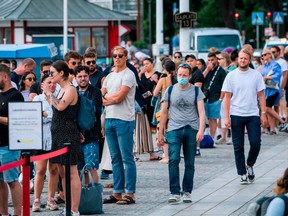 A man wearing a protective mask walks next to travellers as they queue up to board a boat at Stranvagen in Stockholm on July 27, 2020, during the novel coronavirus / COVID-19 pandemic.