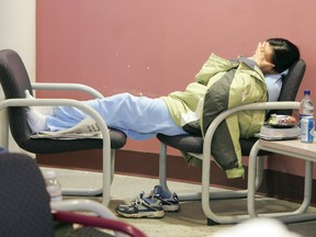 A woman stretches out across two chairs and under a jacket with her shoes off as she waits in the waiting room at the University of Alberta Hospital Emergency Room.