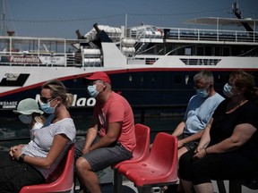 Tourists with masks sit on a leisure boat on the Aegean island of Rhodes on August 29, 2020, amid the COVID-19 novel coronavirus outbreak. Rhodes island, one of the mass tourism Greek islands is popular with British tourists.