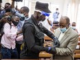"Hotel Rwanda" hero Paul Rusesabagina, right, is handcuffed by a police officer after his pre-trial court session at the Kicukiro Primary court in Kigali, Rwanda, on Sept. 14.