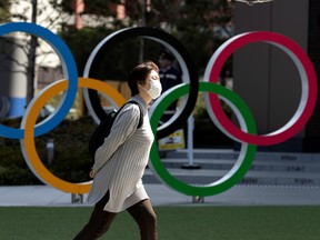 A woman wearing a protective face mask walks past the Olympic rings in front of the Japan Olympics Museum in Tokyo amid the coronavirus disease (COVID-19) pandemic, March 13, 2020.