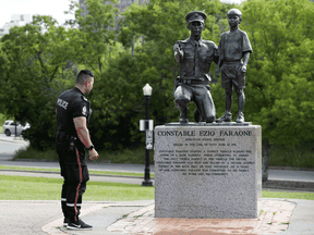 A police officer visits the statue of Constable Ezio Faraone in Constable Ezio Faraone Park after it was vandalized with spray paint, in Edmonton Friday Sept. 4, 2020. The spray paint was quickly removed.