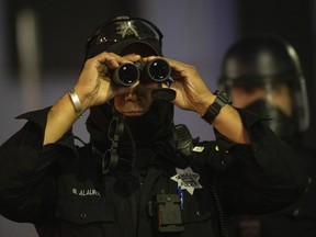 A police officer surveils protesters with binoculars during a protest on Saturday, July 25, 2020, in Oakland, Calif. Police forces across Canada have already begun using technology to predict who may become involved in illegal activity or where crimes might take place, an expert group warned Tuesday as it called on the federal government to protect residents from the potential perils of such tactics.