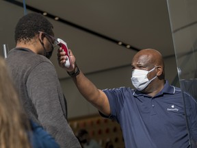 A security guard wearing a protective mask uses a digital thermometer to take the temperature of a customer outside an Apple store in San Francisco, on Oct. 23.