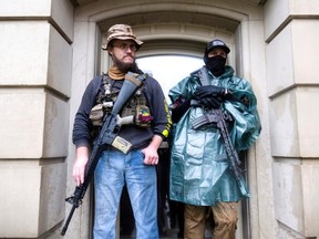 Protesters with long guns shelter from the heavy rain during a protest against Governor Gretchen Whitmer's extended stay-at-home orders at the Capitol building in Lansing, Michigan, U.S. May 14, 2020. PHOTO BY SETH HERALD/REUTERS.