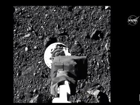 This NASA video frame grab handout image obtained on October 21, 2020 shows NASA's robotic arm from spacecraft Osiris-Rex making contact with asteroid Bennu to collect samples.