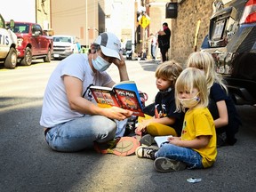 A family reads a book as they sit in an alleyway for hours at a COVID assessment centre at St. Michael's Hospital during the COVID-19 pandemic in Toronto on Monday, September 28, 2020.