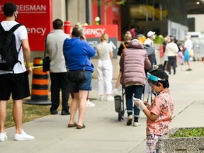 A young boy plays on a phone as he waits in line at a COVID assessment centre at Mount Sinai Hospital during the COVID-19 pandemic in Toronto on Thursday, September 24, 2020.