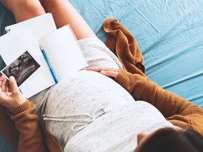 Pregnant woman makes notes, looking at ultrasound image and medical documents.