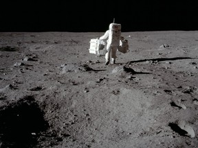 Lunar module pilot Buzz Aldrin carries a seismic experiments package in his left hand and the Laser Ranging Retroreflector to the deployment area on the surface of the moon at Tranquility Base, July 20, 1969.