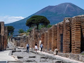 In this file photo taken on May 26, 2020 Visitors walk across the archeological site of Pompeii at the bottom of the Mount Vesuvius volcano (Rear), as the country eases its lockdown aimed at curbing the spread of the COVID-19 infection, caused by the novel coronavirus.