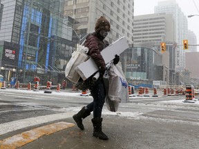 A shopper carries Christmas purchases a day before coronavirus disease (COVID-19) restrictions are reintroduced to regions of the Greater Toronto Area (GTA) as snow falls in midtown Toronto, Ontario, Canada November 22, 2020.