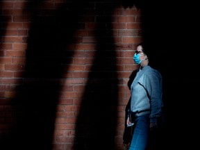 A pedestrian wearing a mask walks through pockets of light on Toronto's Adelaide Street on Monday, November 9, 2020.