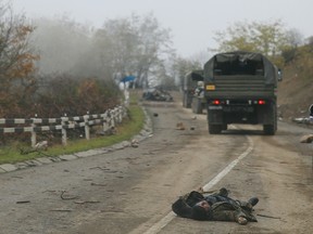 Military vehicles of the Russian peacekeeping forces drive by the body of a person in military uniform, who was killed during a conflict over the breakaway region of Nagorno-Karabakh.