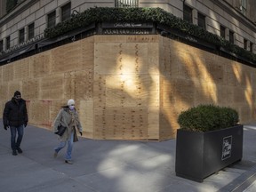 Pedestrians walk past the boarded up windows of a Saks Fifth Avenue department store in New York, on Oct. 31.