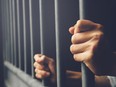 Man in prison hands of behind hold Steel cage jail bars. offender criminal locked in jail.