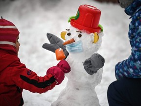 Children play with a snow man wearing a face mask is seen in a playground in Moscow on November 23, 2020.